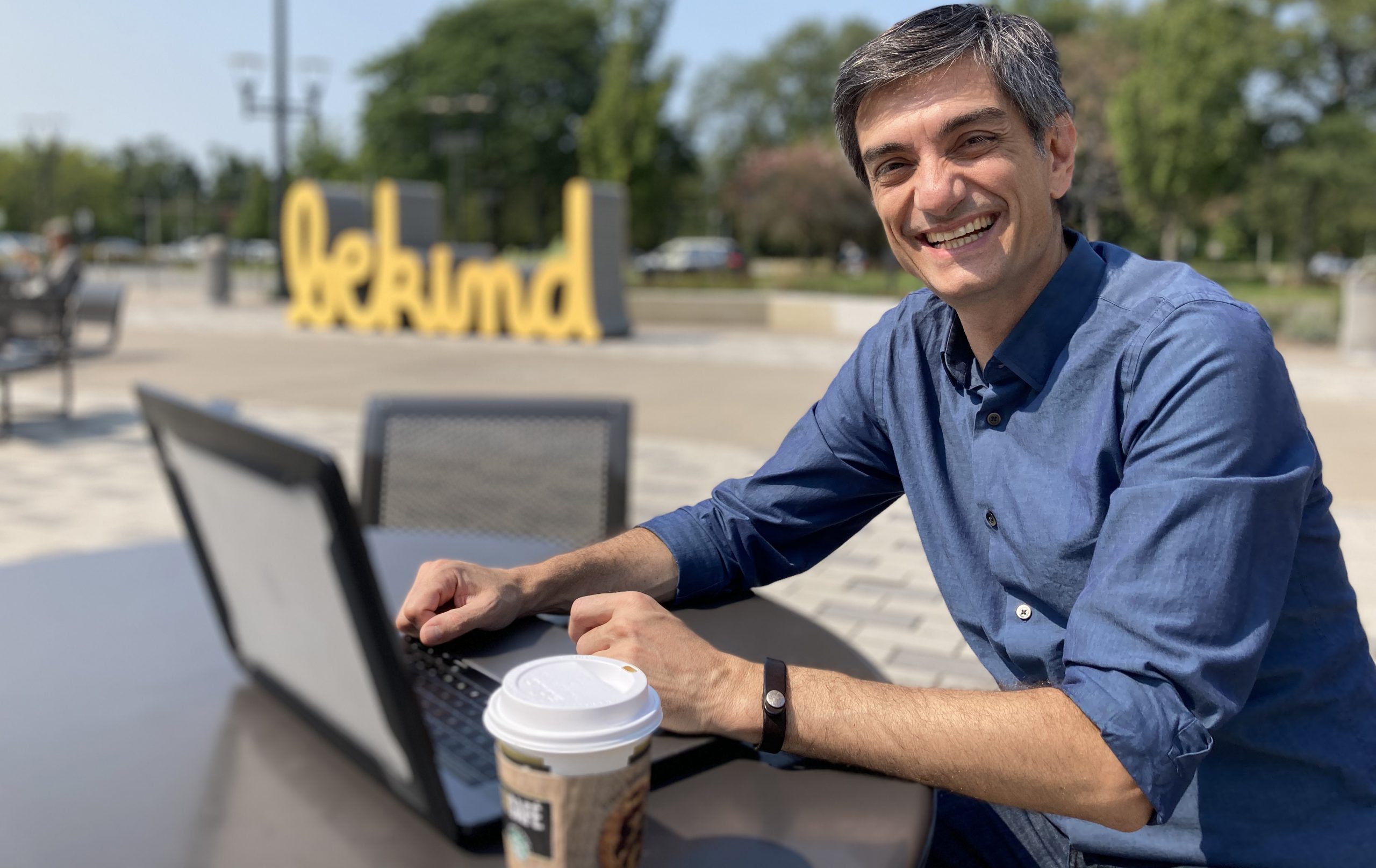 John Scamardella sitting at an outdoor food court with laptop and coffee